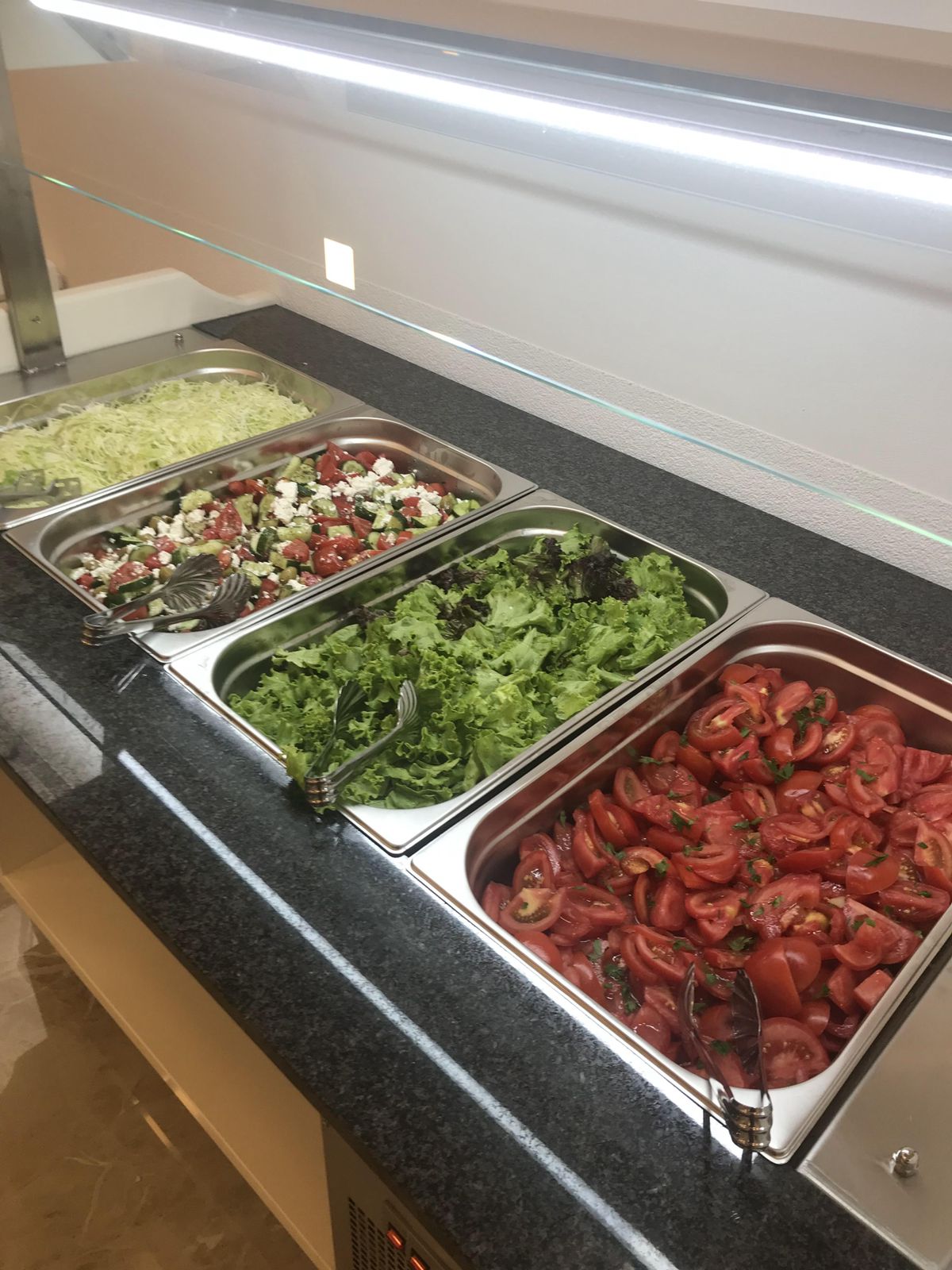 Experience Ulcinj living with modern buffet amenities&mdash;fresh salads served on stainless trays, ideal for real estate in Montenegro.