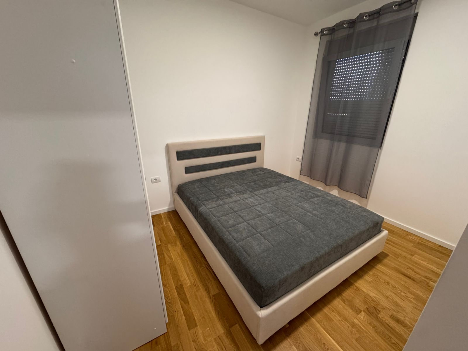 Modern Ulcinj bedroom: double bed, stylish grey headboard, wood floors, ample wardrobe. Invest in Montenegro; eksophere doo project.