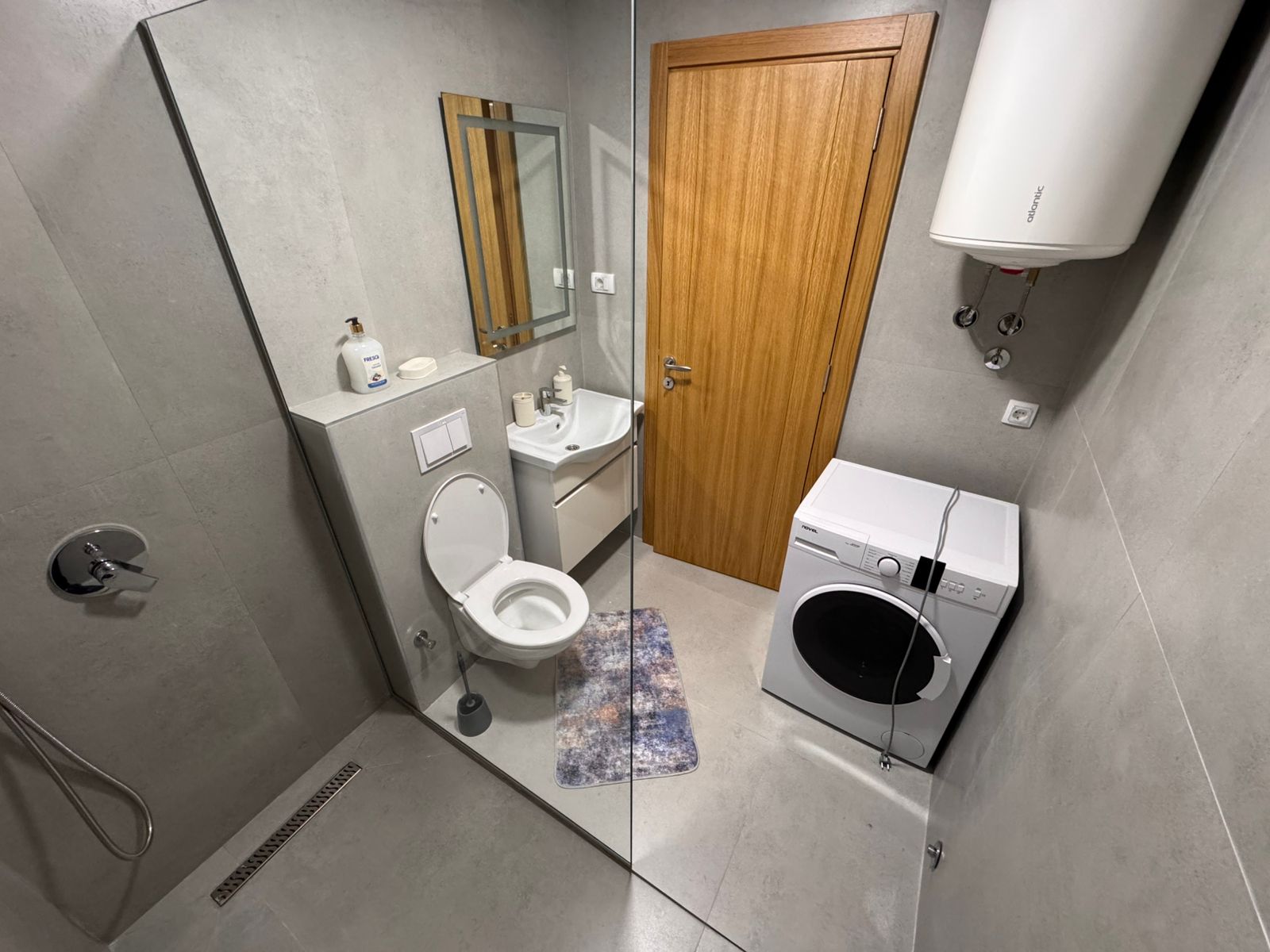Modern Ulcinj bathroom: sleek gray tiles, premium fixtures, washing machine&mdash;ideal Montenegro investment via ekosphere doo.