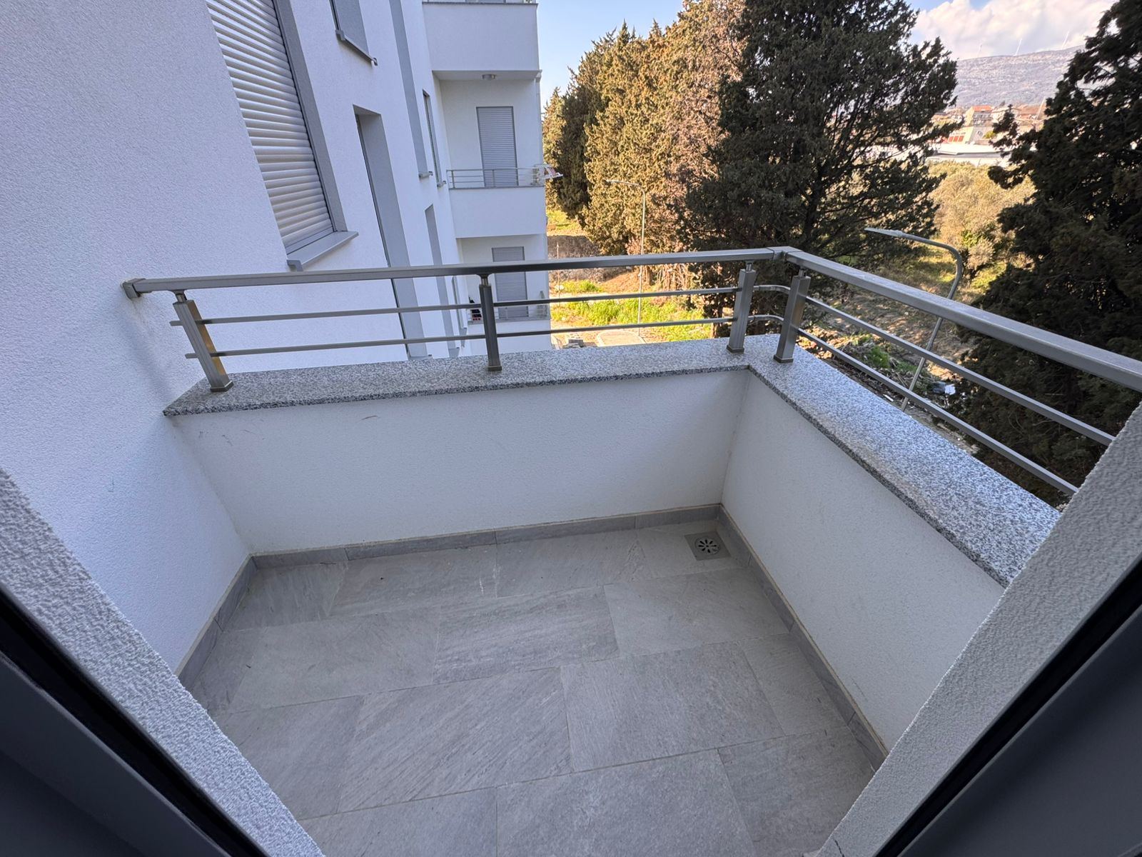 Modern balcony with light tile floor, metal railings, and lush greenery views&mdash;ideal Ulcinj investment. Exclusive at montenegro-listings.me by ekosphere doo.