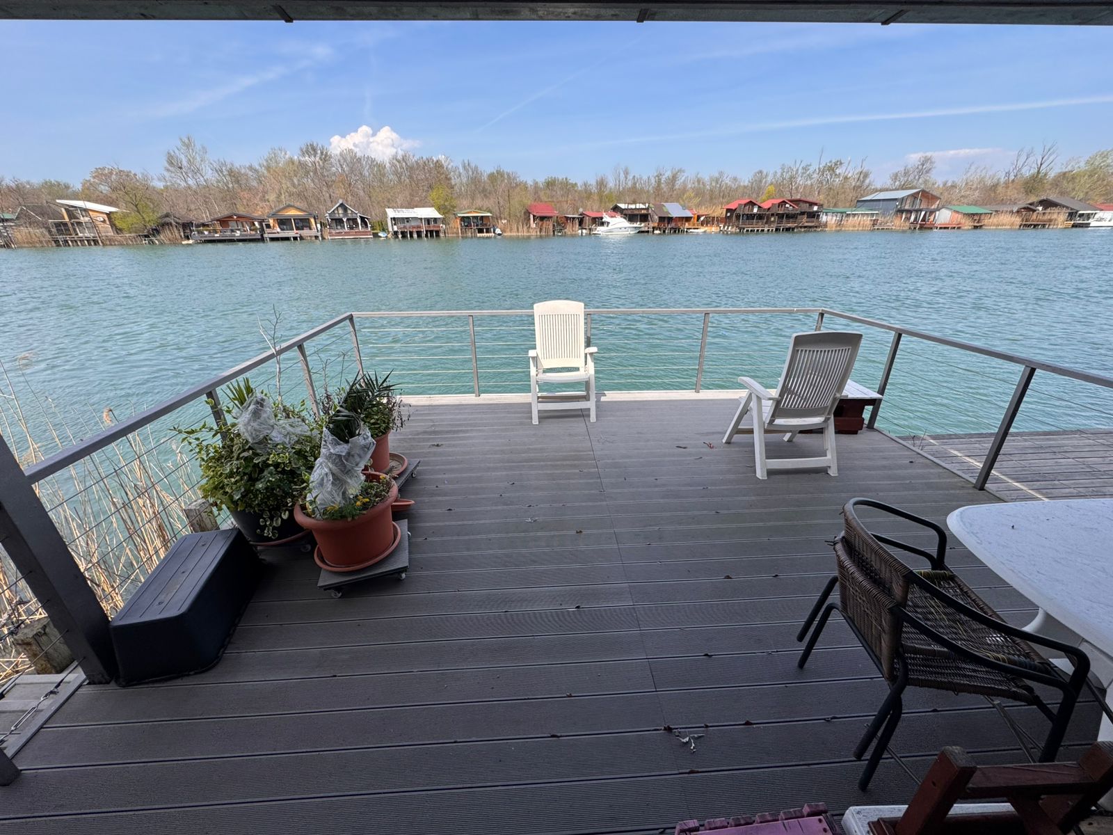 Stunning Ulcinj lakeside deck: lounge chairs, lush potted plants, water views of charming homes. Invest with Montenegro-Listings.me by ekosphere doo.