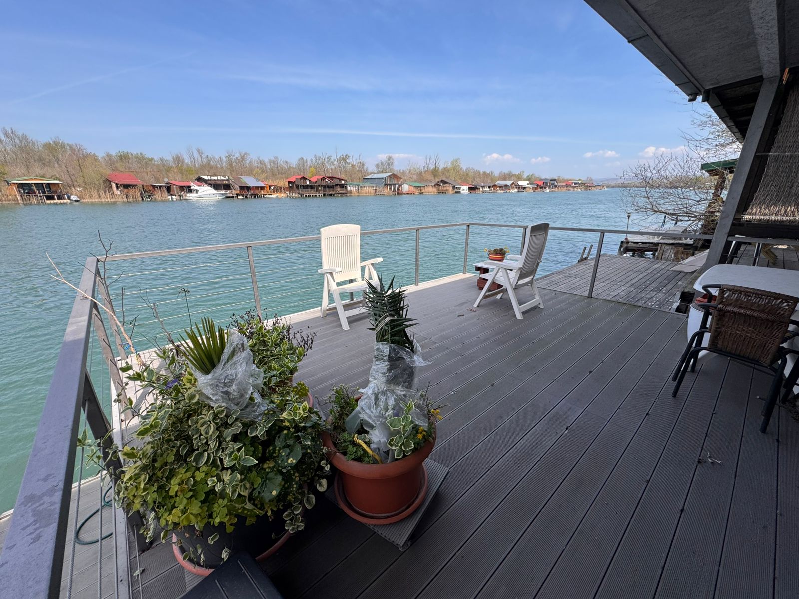 Charming Ulcinj riverfront deck with potted plants, white chairs, and table; stunning red-roof views&mdash;invest via montenegro-listings.me.