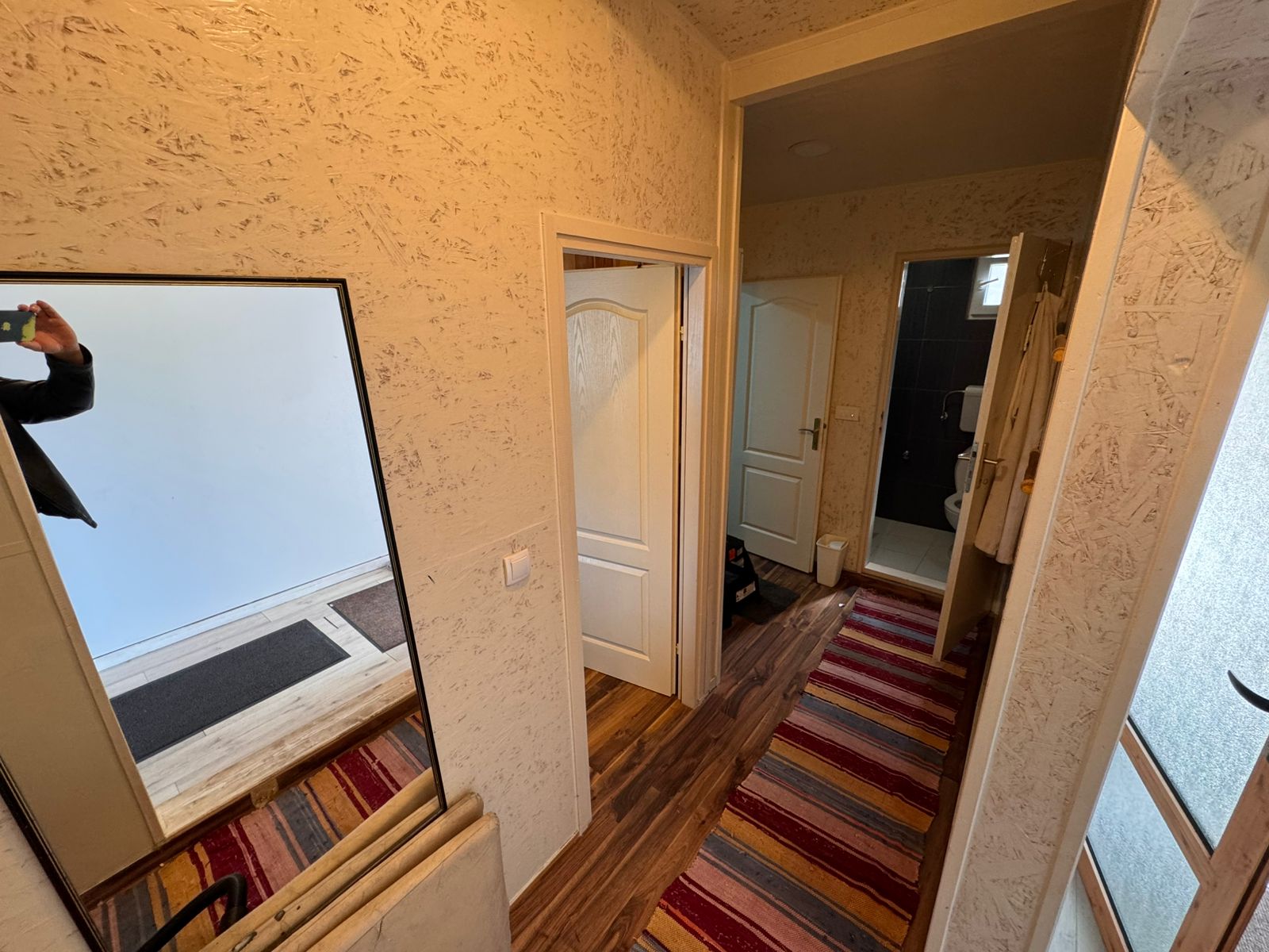 Modern Ulcinj hallway with textured beige walls, striped rug, and stylish entry to a tiled bathroom&mdash;exclusive at montenegro-listings.me.