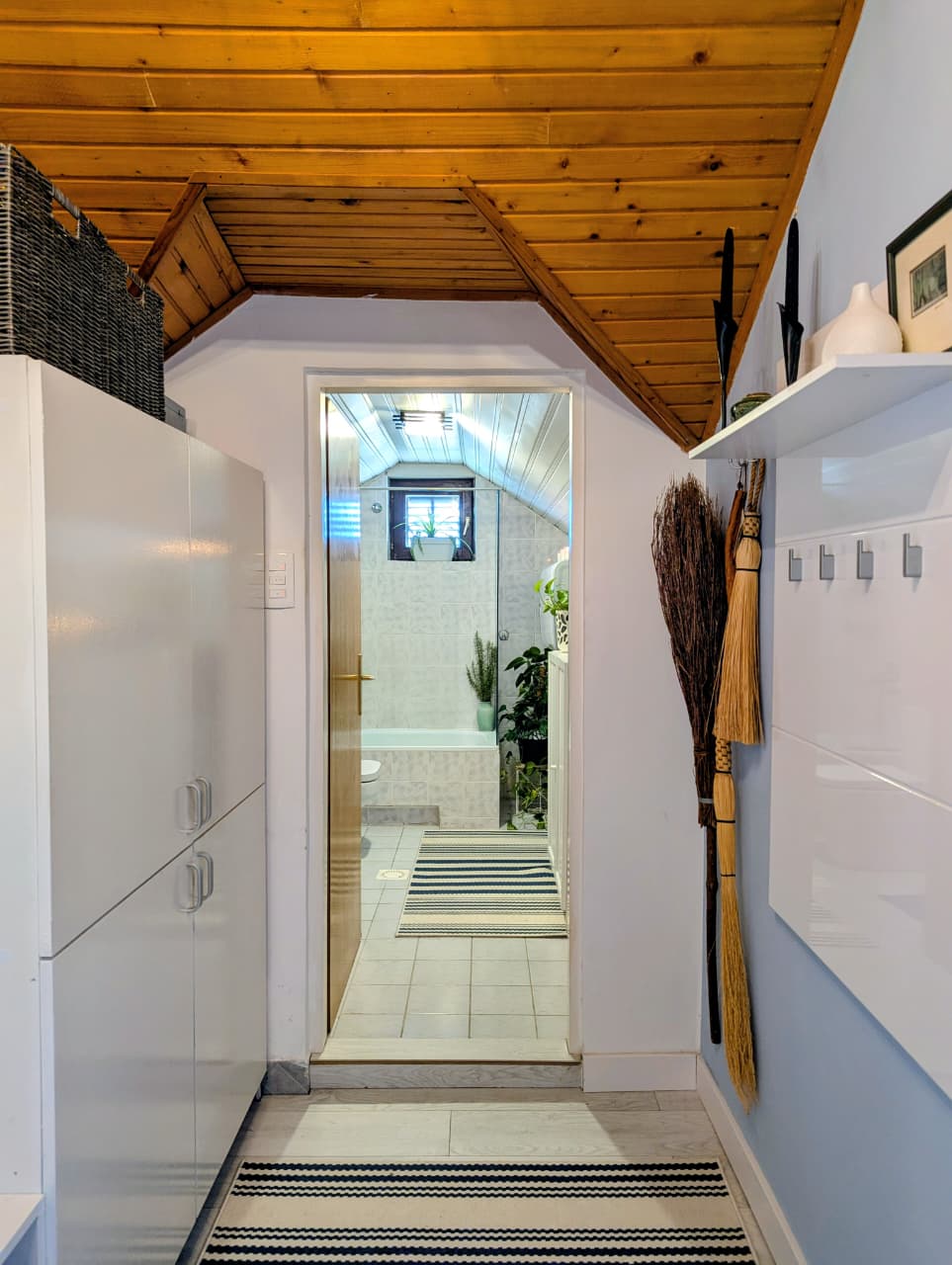 Modern hallway in Ulcinj home: white cabinets, striped rug, wood ceiling; leads to tiled bathroom. Invest at montenegro-listings.me by ekosphere doo.