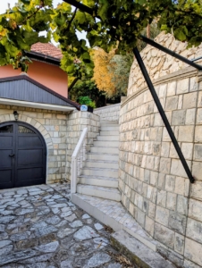 Elegant stone staircase with classic white railings and lush greenery, near a pink home—prime Ulcinj real estate by ekosphere doo.