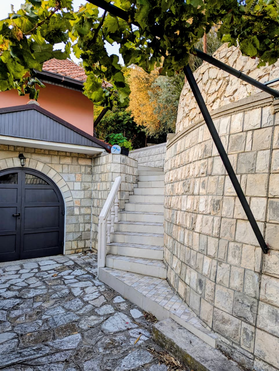 Elegant stone staircase with classic white railings and lush greenery, near a pink home&mdash;prime Ulcinj real estate by ekosphere doo.
