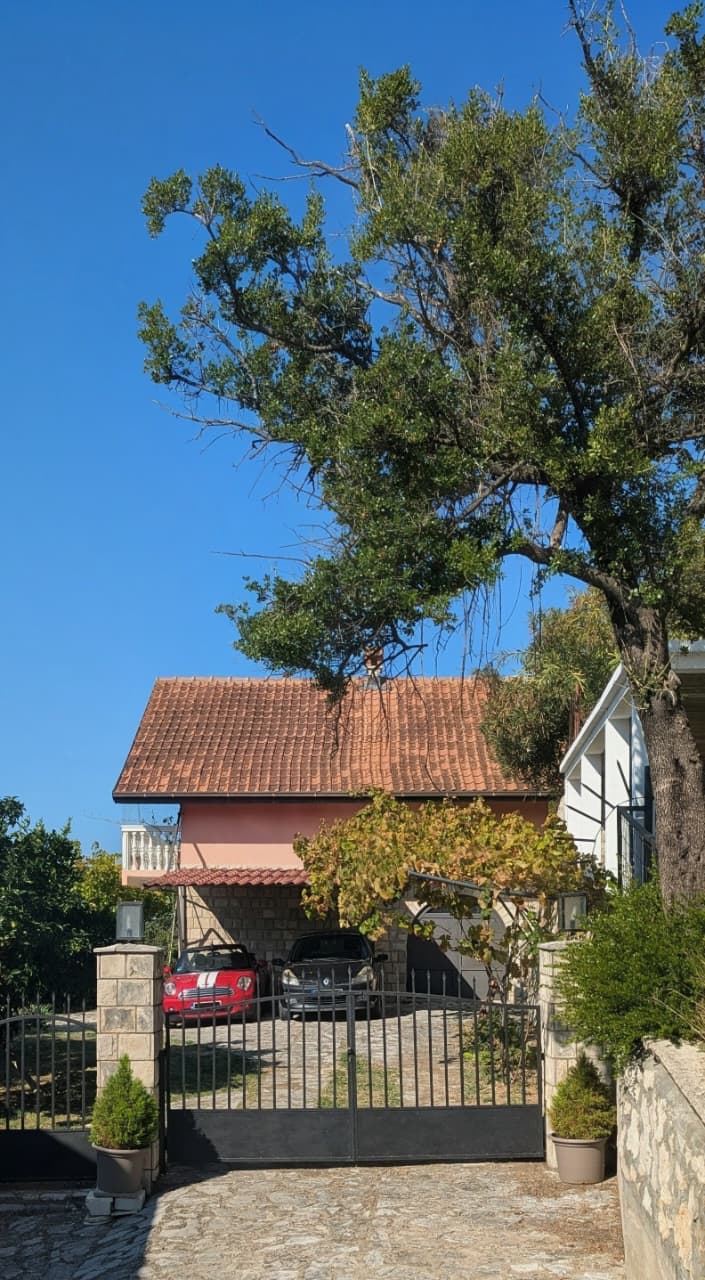 Exclusive Ulcinj property: Gated driveway, red-tiled roof, carport, lush greenery. Invest with montenegro-listings.me by ekosphere doo.