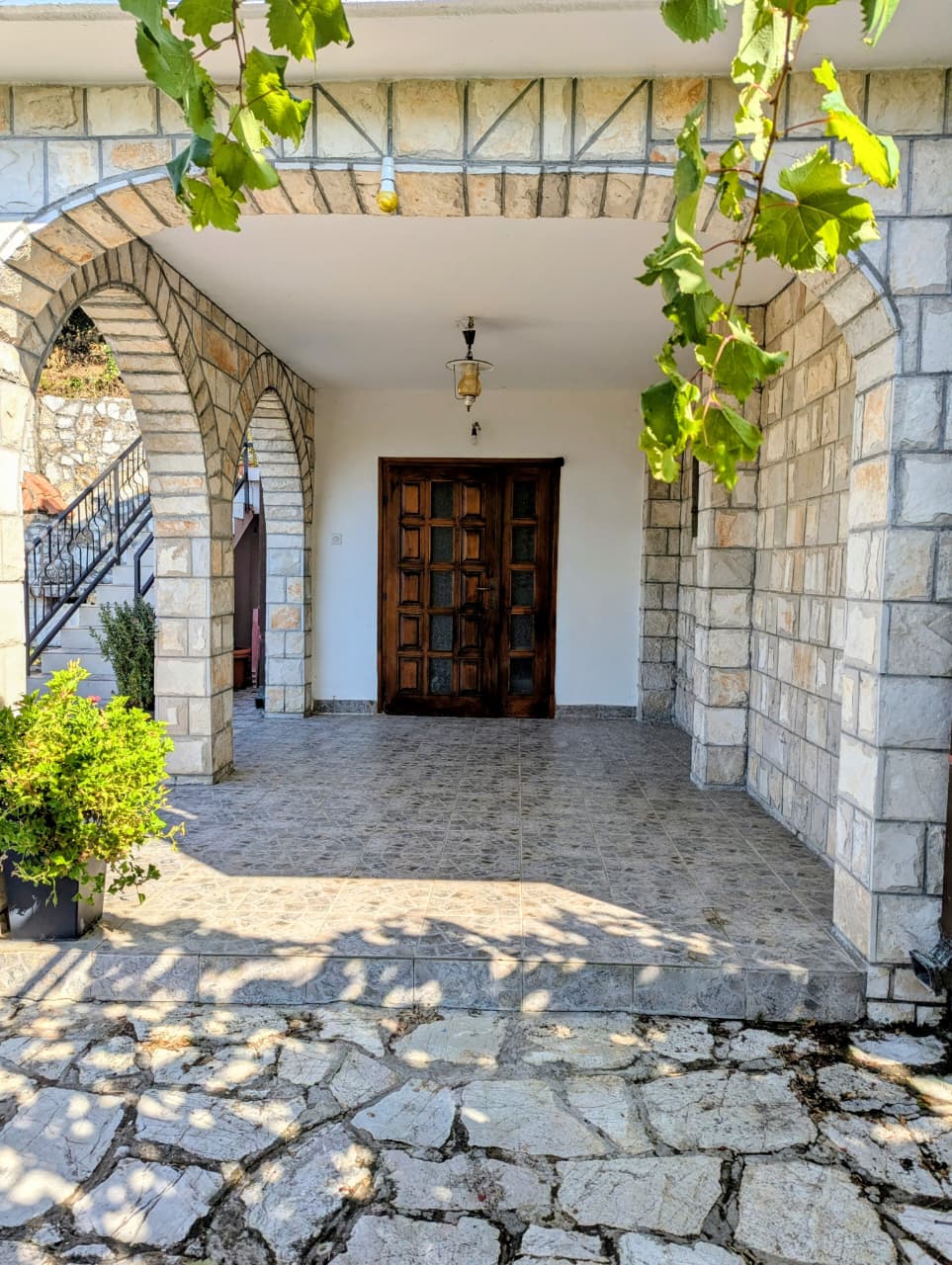Elegant stone-tiled porch with arches and double wooden doors, lush vines, and potted plants&mdash;perfect Ulcinj investment. Montenegro-listings.me by ekosphere doo.