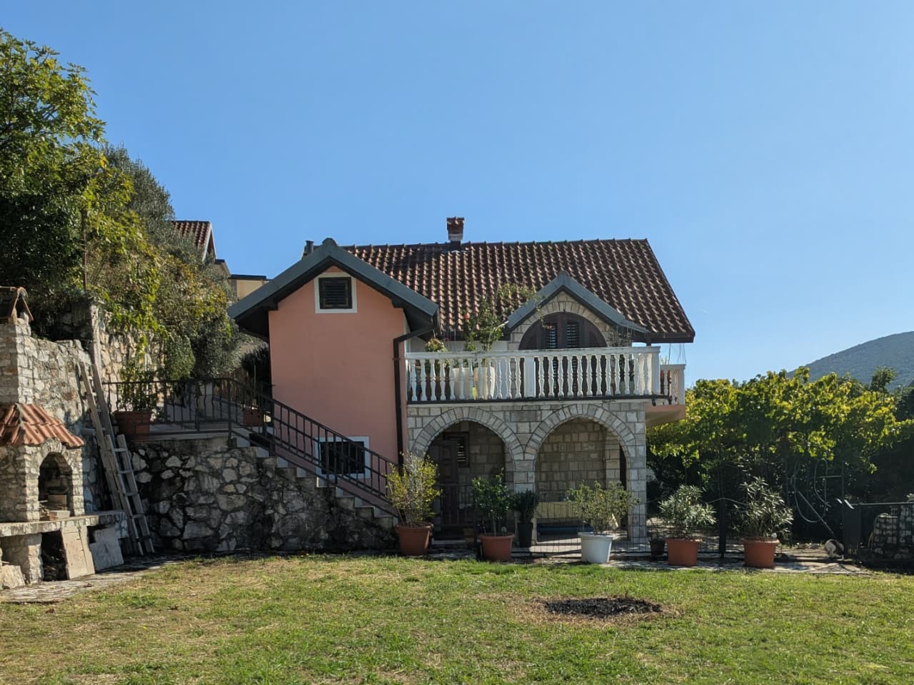 Elegant two-story Ulcinj home with red-tiled roof, balcony, stone arches, lush yard, grill&mdash;invest with montenegro-listings.me by ekosphere doo.