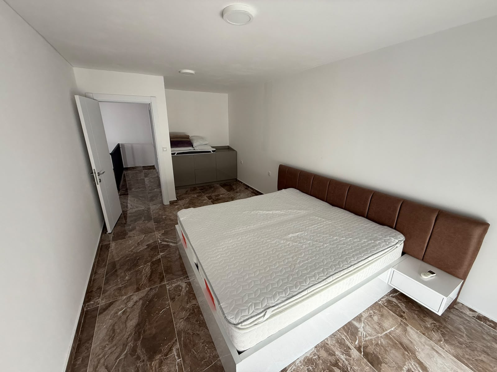 Spacious Ulcinj bedroom features a modern bed, stylish headboard, tiled floors&mdash;ideal Montenegro investment from ekosphere doo.