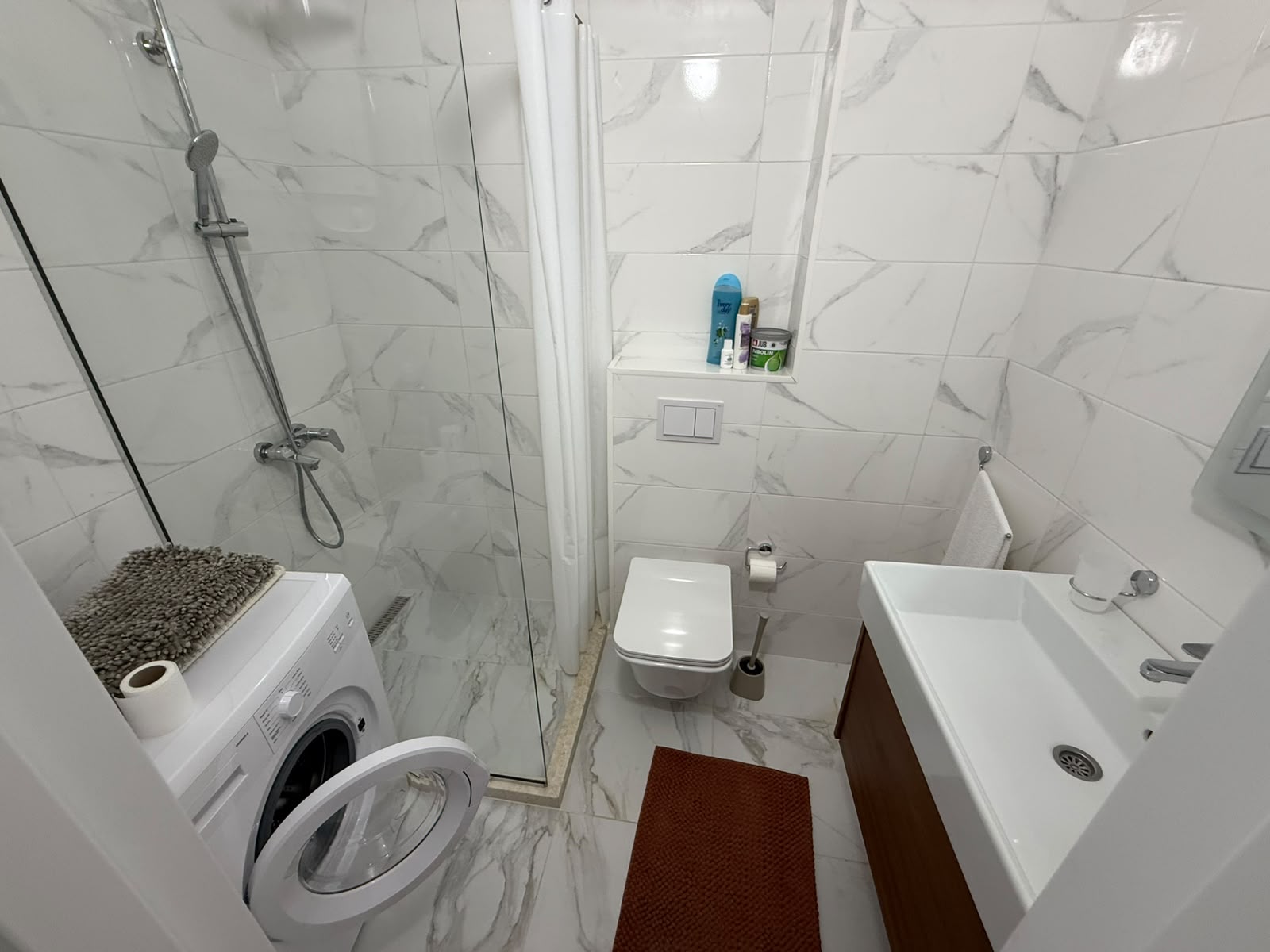 Modern Ulcinj bathroom with marble-style tiles, glass shower, washing machine, and sleek fixtures&mdash;exclusive at montenegro-listings.me.