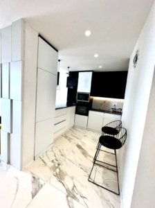Sleek Ulcinj kitchen: white cabinets, marble tiles, black appliances. Luxury investment with montenegro-listings.me by ekosphere doo.