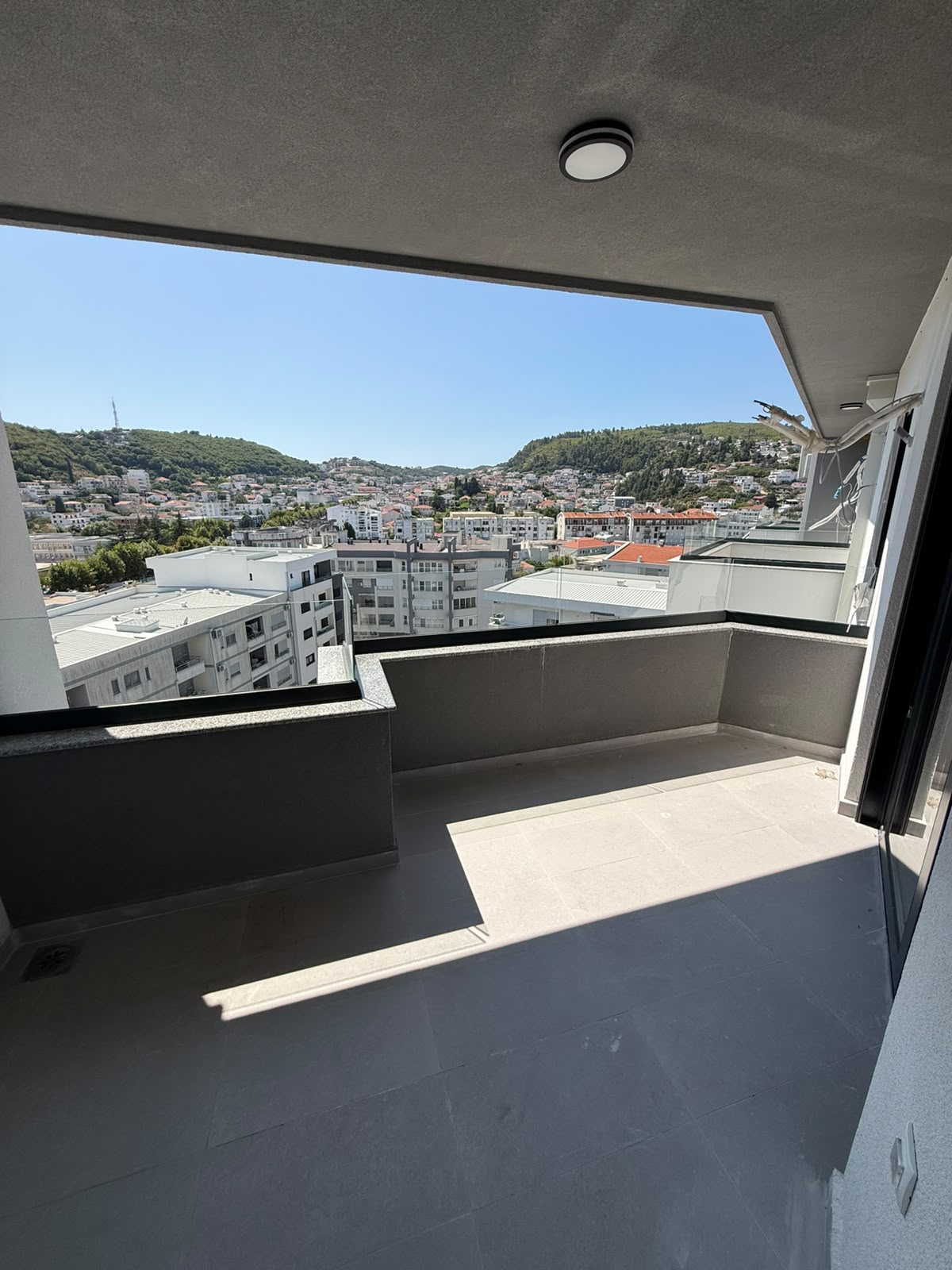 Experience luxury living in Ulcinj, Montenegro with this expansive balcony featuring contemporary gray tiles and panoramic views of the vibrant city skyline, lush tree-covered hills, and clear blue skies. Perfect for investors seeking prime real estate or buyers looking for a serene retreat in one of Montenegro’s most promising property markets. Discover your next investment opportunity at montenegro-listings.me—a premier project by ekosphere doo in Ulcinj.