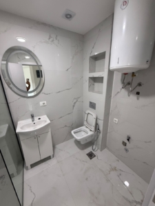 Discover a stylish, modern bathroom featuring elegant white marble tiles in this prime Ulcinj real estate opportunity. Enjoy sophisticated amenities such as a sleek round mirror above the contemporary sink, a wall-mounted toilet for optimal space and comfort, state-of-the-art electric water heating, and thoughtfully designed built-in shelving for ultimate functionality. This clean and minimally furnished space is perfect for investors seeking high-value property in Montenegro’s fast-growing market. Presented by montenegro-listings.me—a project of ekosphere doo in Ulcinj—this property combines luxury finishes with profitable investment potential on the Adriatic coast.