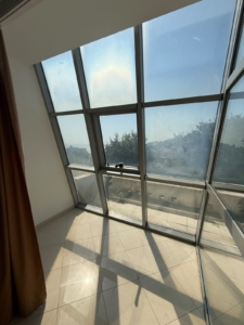 Experience abundant natural light in this spacious, sun-drenched room featuring striking slanted glass windows and elegant tiled flooring—an ideal canvas for your dream home or investment property in Ulcinj, Montenegro. Gaze out through expansive windows that frame lush greenery and the clear blue sky, creating a serene atmosphere enhanced by sophisticated brown curtains. Perfectly situated to maximize sunlight and stunning views, this pristine space offers exceptional potential within the thriving Ulcinj real estate market. Explore exclusive listings at montenegro-listings.me—a trusted project of ekosphere doo—and discover top investment opportunities in Montenegro’s most sought-after locations.