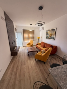 Experience contemporary coastal living in this beautifully designed Ulcinj apartment, exclusively available on montenegro-listings.me—a project of ekosphere doo. The spacious modern living room features elegant wood flooring, vibrant orange and yellow accent chairs, and a stylish coffee table—perfect for relaxing or entertaining guests. Enjoy the sleek wall-mounted TV, tasteful floor lamp, and captivating ship painting that add to the sophisticated ambiance. A large window fitted with striped blinds floods the space with natural light while offering scenic views—an exceptional real estate investment opportunity in Montenegro’s thriving property market.