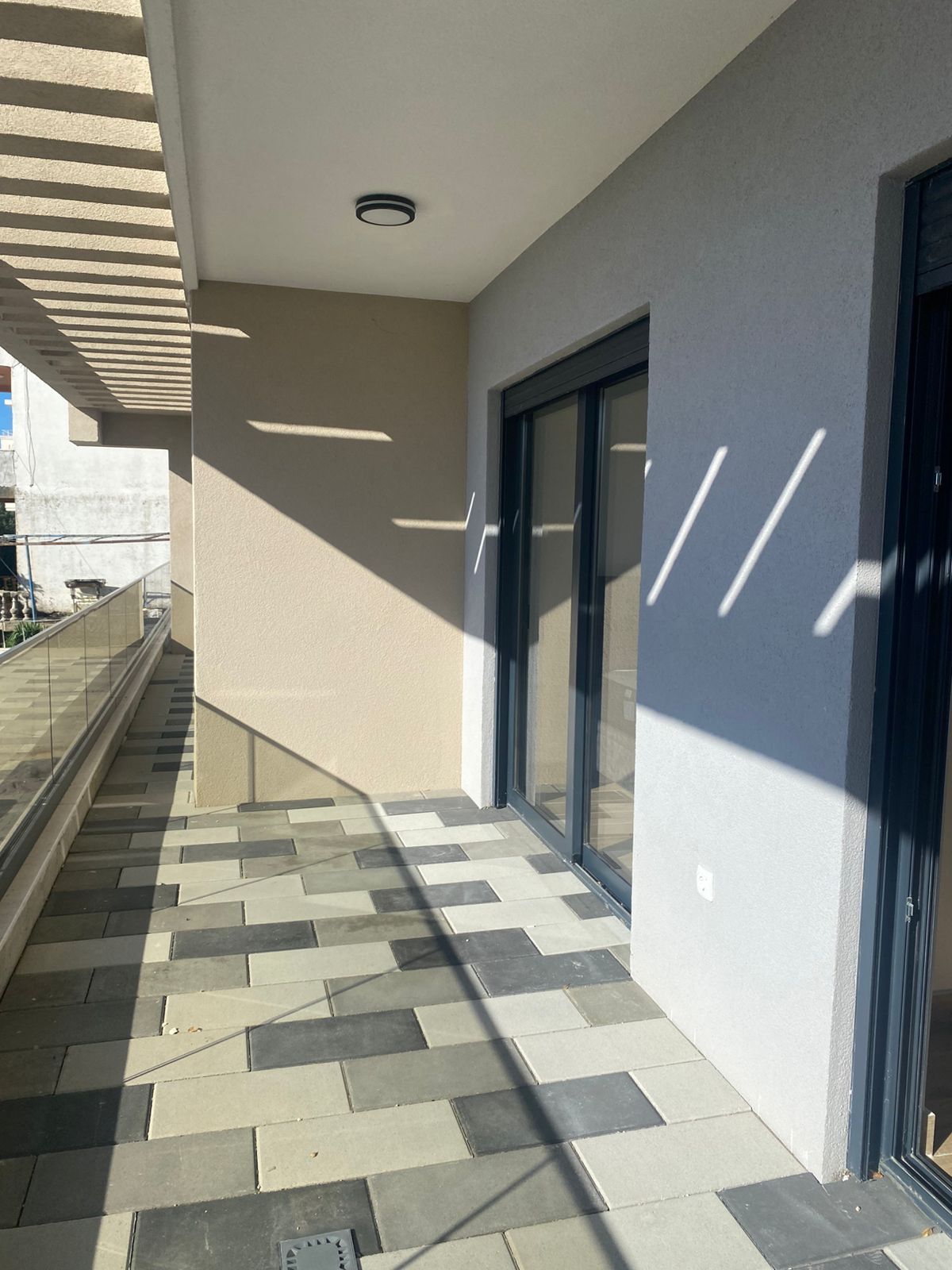 Experience modern coastal living with this elegant tiled balcony in Ulcinj, Montenegro, featuring sleek glass railings and expansive sliding glass doors that invite abundant natural light. The contemporary pergola casts striking geometric shadows across the spacious terrace, enhancing both privacy and aesthetic appeal—perfect for relaxation or entertaining guests. This sun-drenched outdoor space is an excellent investment opportunity in the thriving Montenegro property market. Discover premium real estate options on montenegro-listings.me—a project of ekosphere doo in Ulcinj—where luxury meets prime location.