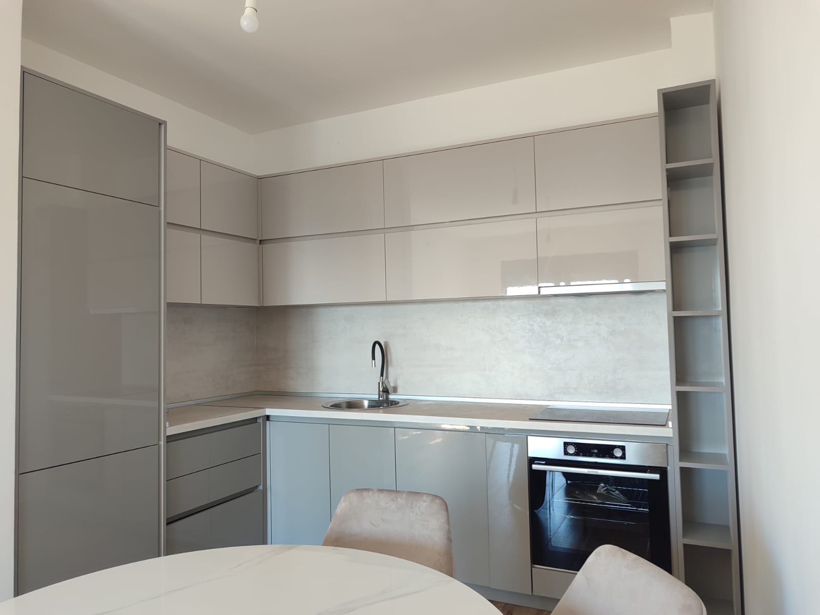 Experience contemporary living in Ulcinj, Montenegro with this stunning modern kitchen, featuring elegant grey cabinets, premium built-in oven, advanced induction cooktop, and a sleek integrated sink. The open shelving adds both style and functionality. Enjoy dining at the stylish round white table surrounded by chic beige chairs. Designed with a minimalist aesthetic and neutral color palette, this space perfectly suits discerning buyers seeking high-quality real estate or lucrative property investment opportunities in Ulcinj. Discover exclusive listings on montenegro-listings.me—a project of ekosphere doo—and invest in your dream home today.
