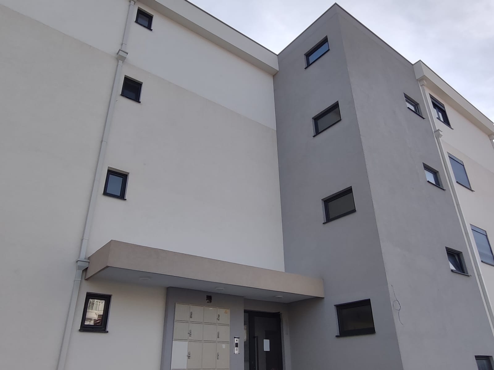 Discover this contemporary apartment building in Ulcinj, Montenegro, featuring a stylish combination of white and gray exterior walls and modern rectangular windows. The property boasts a secure covered entrance and convenient mailboxes near the main door, exemplifying both comfort and functionality—ideal for investors seeking high-quality real estate opportunities in Ulcinj. Perfectly suited for residential living or rental income potential, this property listing on montenegro-listings.me—a project by ekosphere doo—offers exceptional investment value in the thriving Montenegro property market.