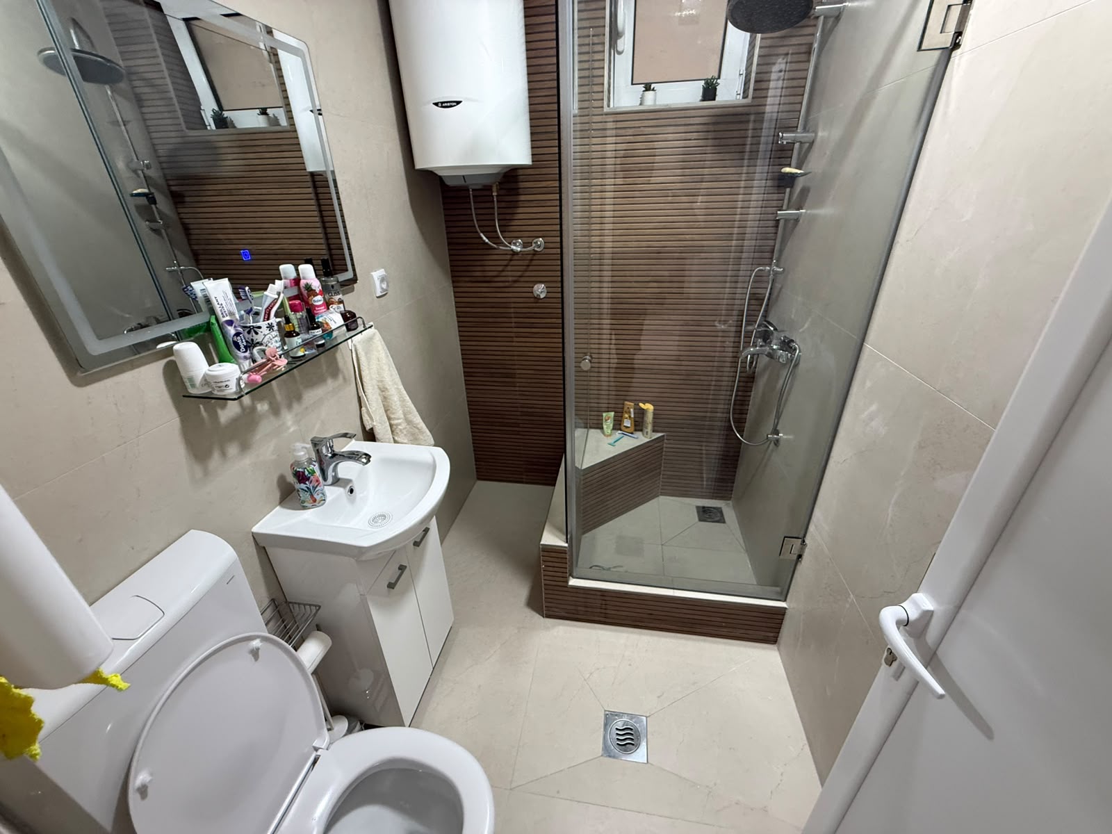 Modern, efficient bathroom in a sought-after Ulcinj property—perfect for investment or year-round living. This well-appointed space features a stylish enclosed glass shower with elegant wooden paneling, a wall-mounted water heater, and convenient storage for toiletries. The room is finished with premium beige tiling and offers essentials including a contemporary toilet, compact sink, wall mirror, and towel rack. Located in one of Montenegro’s prime real estate markets, this turnkey bathroom highlights the quality standards delivered by montenegro-listings.me—a premier project of ekosphere doo in Ulcinj—making it an excellent choice for discerning buyers seeking comfort and value on the Adriatic coast.