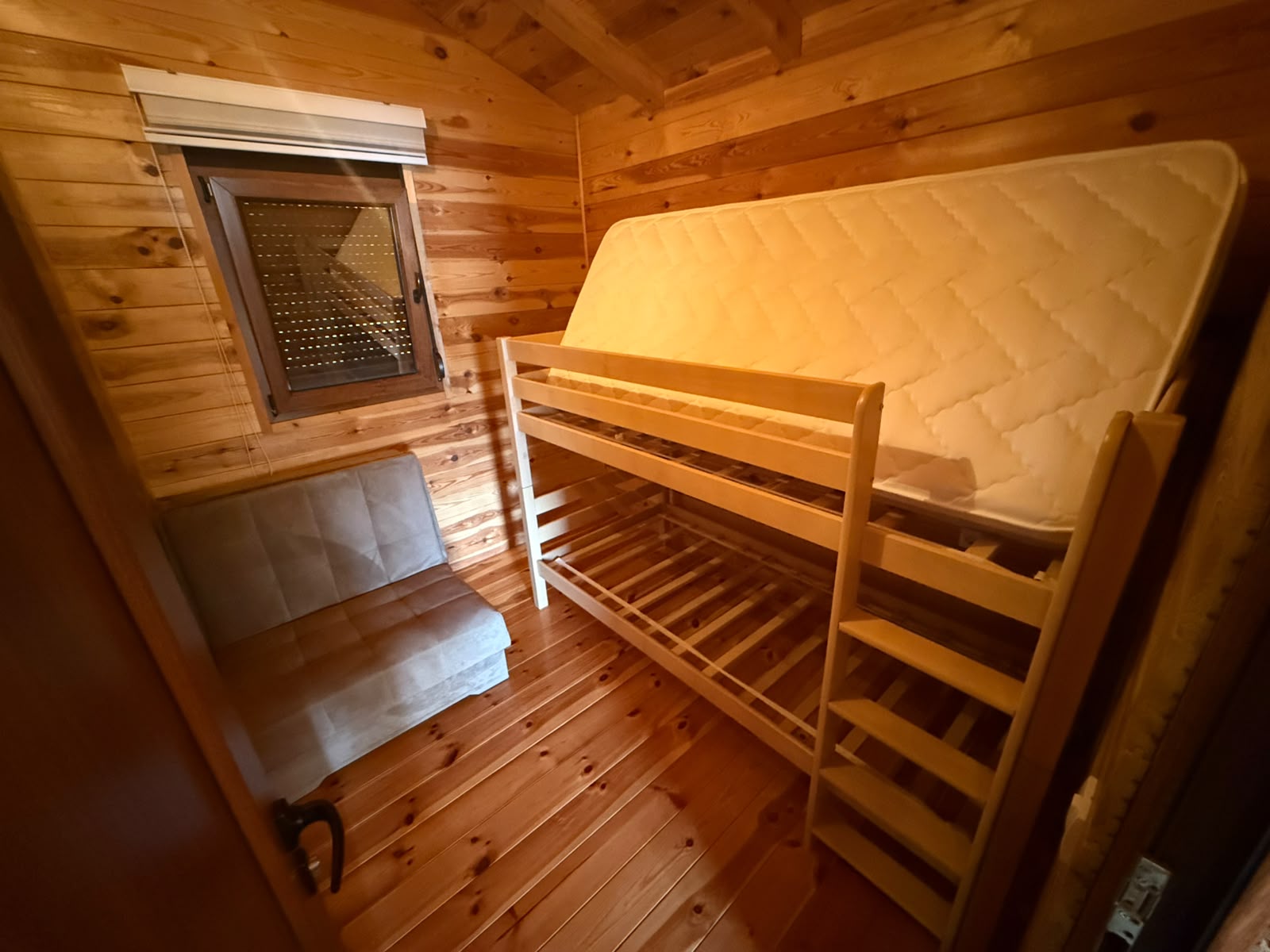 Discover a cozy, well-crafted wooden room for sale in Ulcinj, Montenegro—an excellent real estate opportunity featured on montenegro-listings.me, a trusted project by ekosphere doo. This inviting space boasts warm natural wood floors and panel walls, highlighted by gentle ambient lighting. The room includes a modern bunk bed frame with the mattress conveniently propped on the top level and a stylish gray cushioned seat beneath the generous window. Perfect for rental income or as your private retreat in the heart of Ulcinj’s thriving property market, this charming investment offers comfort and classic Montenegrin character.