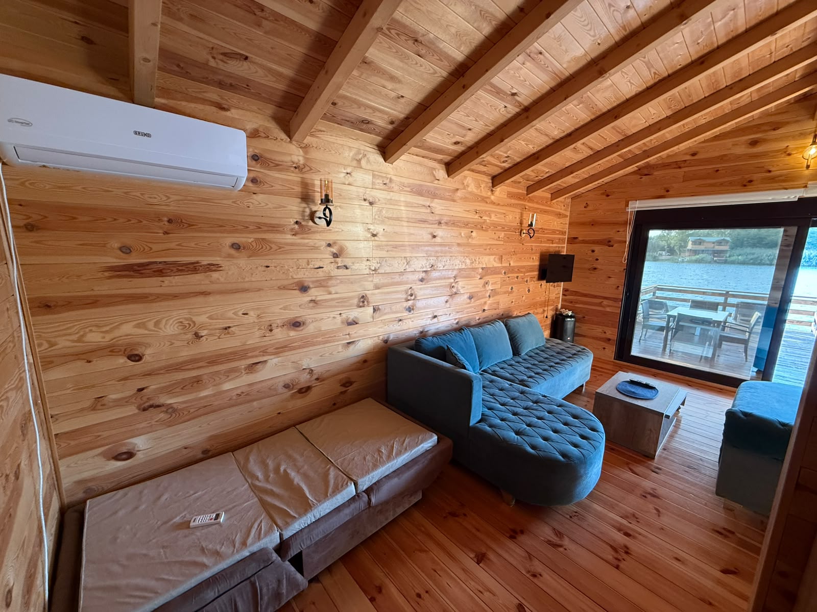 Experience the charm of this inviting wooden cabin for sale in Ulcinj, Montenegro, featuring a stylish blue sectional sofa, modern wall-mounted lighting, efficient air conditioning, and a practical small table. The spacious layout includes a comfortable mattress on the floor—perfect for flexible living arrangements—and boasts a large window offering breathtaking views of tranquil waters and an expansive outdoor deck. This unique property presents an exceptional real estate investment opportunity in Montenegro’s sought-after coastal market. Secure your slice of paradise today through montenegro-listings.me, proudly presented by ekosphere doo Ulcinj.