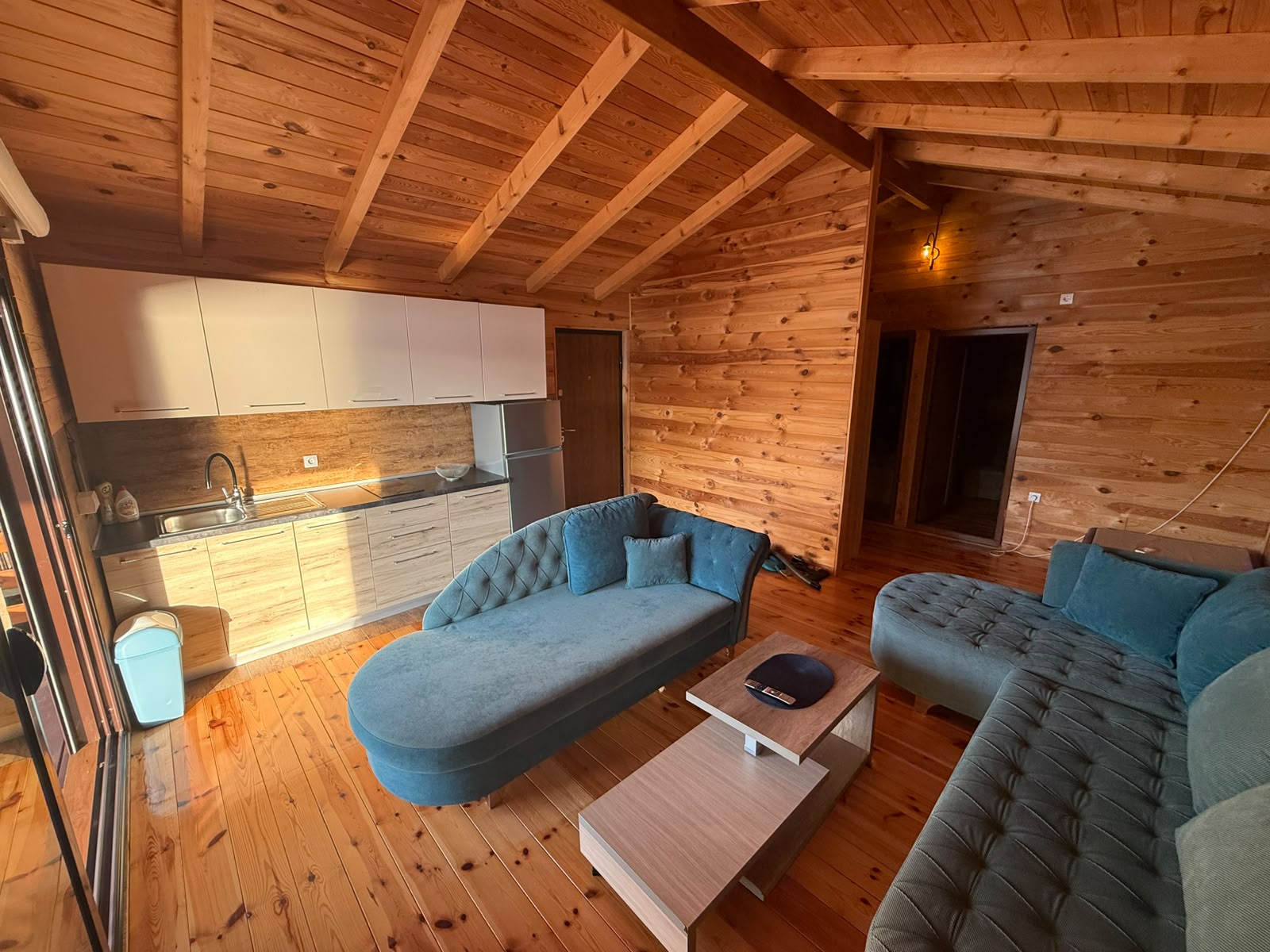 Experience the warmth and inviting atmosphere of this beautifully appointed living room in Ulcinj, Montenegro. Featuring elegant wooden walls and a stylish ceiling, this property boasts spacious blue upholstered sofas perfect for relaxation, a sleek coffee table, and a contemporary kitchenette with premium white cabinetry and stainless steel fixtures. Abundant natural sunlight streams in from the left, enhancing the open-concept layout. An exceptional investment opportunity in the heart of Ulcinj’s sought-after real estate market—discover more exclusive listings at montenegro-listings.me, a trusted project by ekosphere doo.