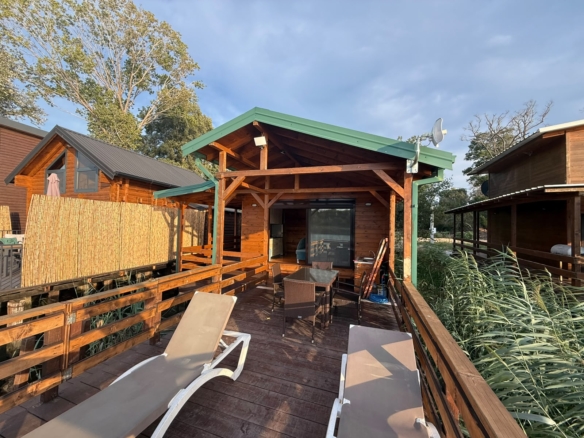 Discover an exceptional investment opportunity in Ulcinj, Montenegro with this charming wooden cabin featuring a distinctive green roof. The property boasts a spacious private deck complete with two comfortable lounge chairs and an outdoor dining area—ideal for relaxing or entertaining guests. Surrounded by lush trees and neighboring cabins, the setting offers natural privacy and tranquility, enhanced by beautiful sunlight filtering through the surroundings. Perfect as a holiday retreat or income-generating rental, this picturesque cabin is showcased exclusively on montenegro-listings.me—a premier project of ekosphere doo in Ulcinj—positioning you at the heart of Montenegro’s thriving real estate market.