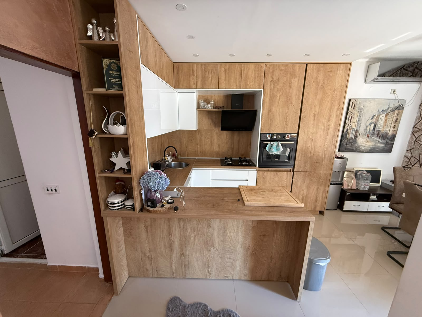 Discover this contemporary kitchen in Ulcinj, Montenegro, featuring elegant wood cabinetry, premium integrated appliances, and a functional small counter with a cutting board—perfect for modern living or discerning investors. Open shelves display stylish décor, dishes, and a classic teapot while seamlessly connecting to a spacious living area ideal for entertaining. Located in one of Montenegro’s most sought-after regions, this property listed on montenegro-listings.me—a project of ekosphere doo—offers exceptional value for both homeowners and real estate investors looking to capitalize on the thriving Ulcinj property market.